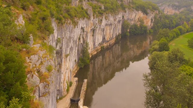 Path of Chemin de Halage along Lot river in Causses du Quercy UNESCO Geopark, France, surrounded by cliffs and greenery.