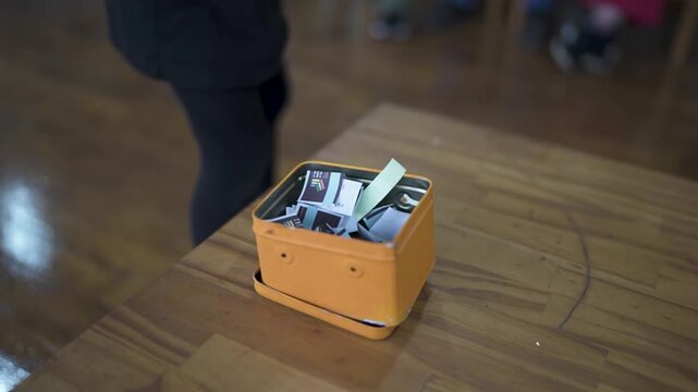 Hand drawing paper from small box during raffle or random selection activity indoors.