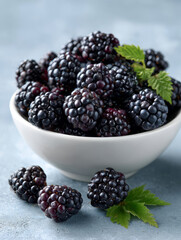 A bowl of fresh blackberries on a textured blue background.