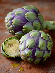 Obraz premium Two whole artichokes and a cut half on a textured surface.