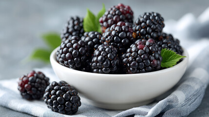 Fresh blackberries in a white bowl with leaves on a cloth.