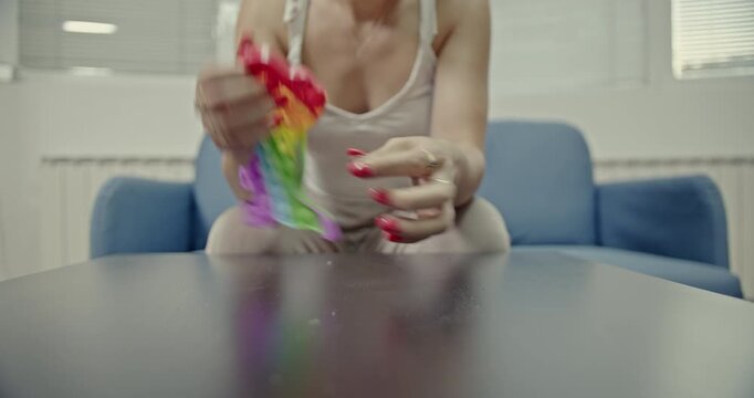 A woman's hands gently press the colorful bubbles of a pop-it fidget toy, creating satisfying and calming sounds. This sensory play offers stress relief and a moment of tranquility.