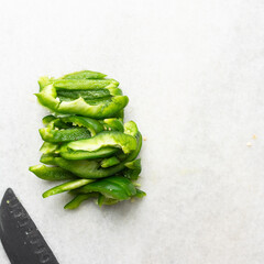 Overhead view of green bell peppers being sliced on a marble countertop, top view of green bell peppers