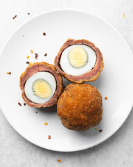 Overhead view of fried scotch eggs on white plate, top view of cross-section of scotch eggs on white dish