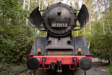 Fototapeta premium Rusting Vintage Steam Locomotive Number 50 3707-2 Surrounded by Dense Green Foliage, Symbolizing the Intersection of Industrial History and Nature's Reclamation in a Tranquil Forest Setting