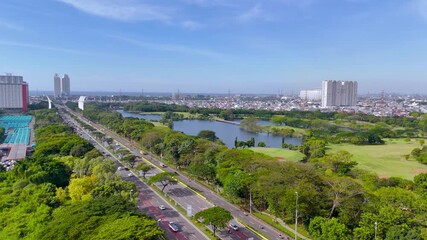 Jakarta, Indonesia - 07 October 2025: Aerial view of city streets, green trees, a lake, and tall buildings, under a clear blue sky.