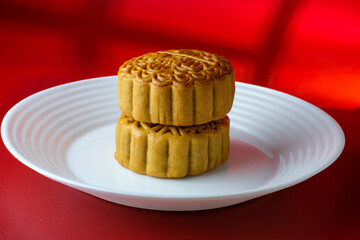 Two traditional mooncakes stacked on a white plate with a red background and soft shadows. Perfect for bakery promotions, or Asian holiday visuals. cultural heritage during the Mid-Autumn Festival
