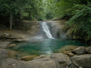 Beautiful tropical waterfall flowing into turquoise lagoon surrounded by lush green forest, peaceful nature landscape with crystal clear water, rocks and sunlight reflections in jungle