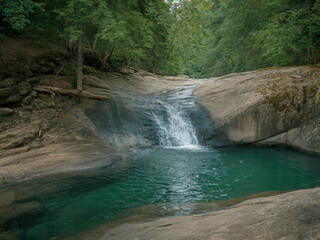 Beautiful tropical waterfall flowing into turquoise lagoon surrounded by lush green forest, peaceful nature landscape with crystal clear water, rocks and sunlight reflections in jungle