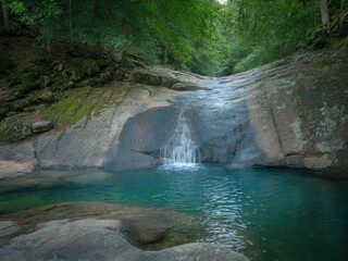 Beautiful tropical waterfall flowing into turquoise lagoon surrounded by lush green forest, peaceful nature landscape with crystal clear water, rocks and sunlight reflections in jungle