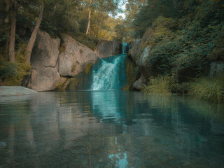 Beautiful tropical waterfall flowing into turquoise lagoon surrounded by lush green forest, peaceful nature landscape with crystal clear water, rocks and sunlight reflections in jungle