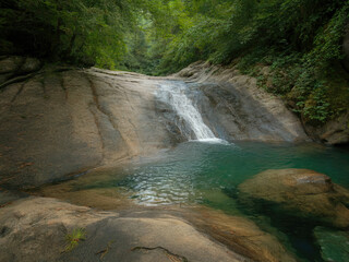 Beautiful tropical waterfall flowing into turquoise lagoon surrounded by lush green forest, peaceful nature landscape with crystal clear water, rocks and sunlight reflections in jungle