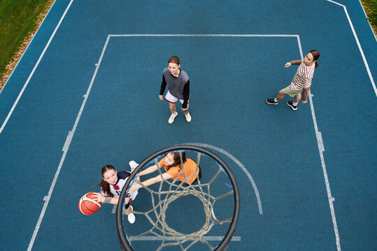 Group of teenage girls playing streetball on outdoor court, Caucasian and Asian teenagers competing for basketball near hoop, teammates and opponents actively participating in game