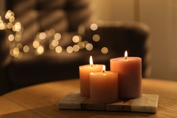 Burning candles on wooden table against blurred lights indoors, closeup. Space for text
