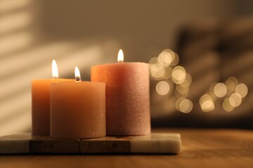 Burning candles on wooden table against blurred lights indoors, closeup. Space for text
