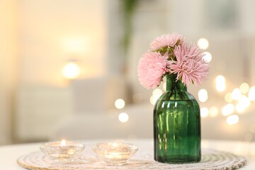 Burning candles and beautiful flowers on white table indoors, closeup with space for text. Bokeh effect