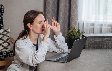Young woman sits at a laptop, looking at the screen with an expression of anticipation or waiting for results.