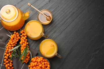 Sea buckthorn tea in glass cups, teapot, fresh berries and honey on black table, flat lay. Space for text