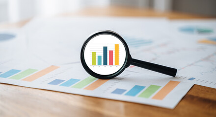 Magnifying glass rests on a table, highlighting economic data and financial charts for detailed analytical research