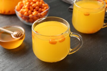 Sea buckthorn tea in glass cups, honey and fresh berries on black table, closeup