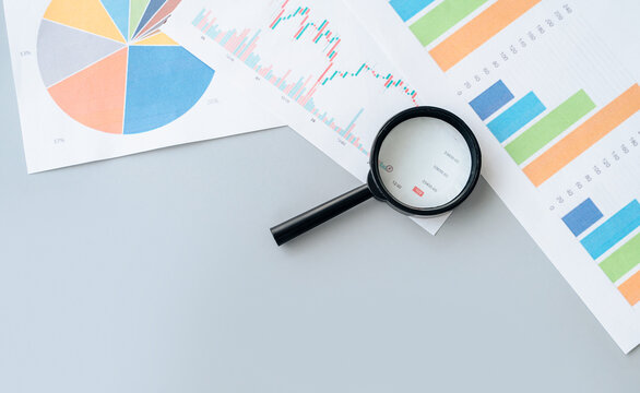 Magnifying glass rests on a table, highlighting economic data and financial charts for detailed analytical research