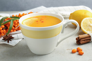 Sea buckthorn tea in cup, spices, lemon and fresh berries on light grey table, closeup