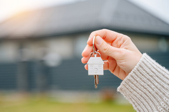 Close-up of a person's hand holding a metal keychain with house keys and a fob against a blurred background