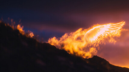 Beautiful orange and purple clouds form an angel wing shape during sunset over a mountain landscape
