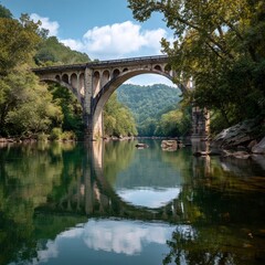 Fototapeta premium A Majestic Arched Concrete Bridge Spanning a Calm River, Creating a Perfect Symmetrical Reflection of the Structure and Surrounding Green Forest in the Still Water.