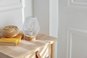 Stylish nightlamp, wicker storage box and book on nightstand near white wall indoors. Space for text