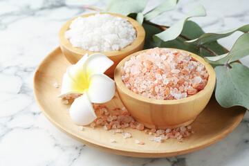 Sea salt, eucalyptus branch and plumeria flower on white marble table, closeup