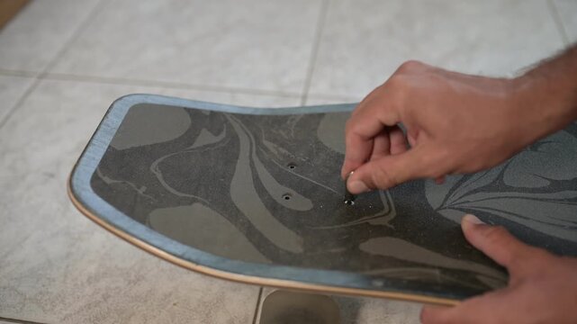 Close-up of a person using an Allen key to assemble or adjust a surfskate, tightening bolts on the grip tape surface of the board