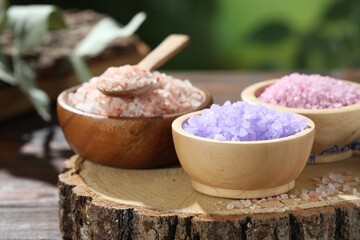 Different types of sea salt on wooden table against blurred background, closeup