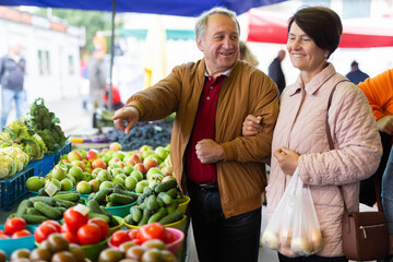 Happy mature male and female picking fresh organic vegetables during shopping at local bazaar