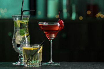Glasses of tasty cocktails on dark table against blurred background, bokeh effect. Space for text