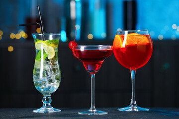 Glasses of tasty cocktails on dark table against blurred background, bokeh effect