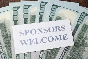 Sponsors Welcome card and dollars on wooden table, top view