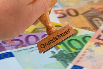 Stempel mit dem Aufdruck "Grundsteuer" vor Geldscheinen