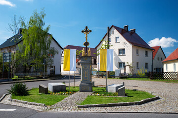 Geschm&uuml;cktes Wegkreuz in einem sorbischen Dorf der Lausitz, mit gelb-wei&szlig;en Kirchenfahnen zur Osterzeit. Zeichen von Glauben, Tradition und katholischem Brauchtum in Sachsen