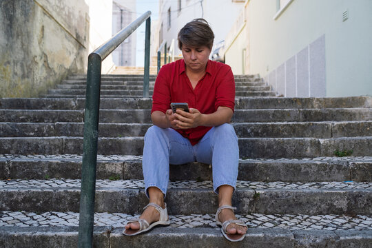 Sad woman sitting on stairs with a phone. no signal, no money, or afraid to call her boyfriend
