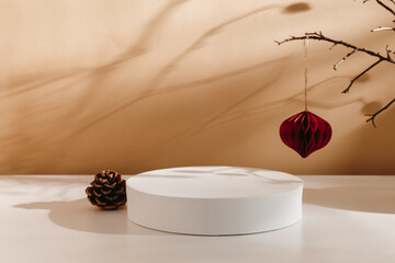 Aesthetic podium with christmas tree cone and paper ball hanging on the branch with beautiful shadows. Christmas showcase for product presentation