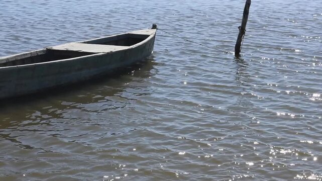 Small boat moored to a rustic wooden pole by rope, gently floating on the calm waters of Narta Lagoon, Albania. Serene coastal landscape with soft natural light and peaceful atmosphere