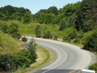 Acurving asphalt road winding through a hilly, green, and heavily treed landscape