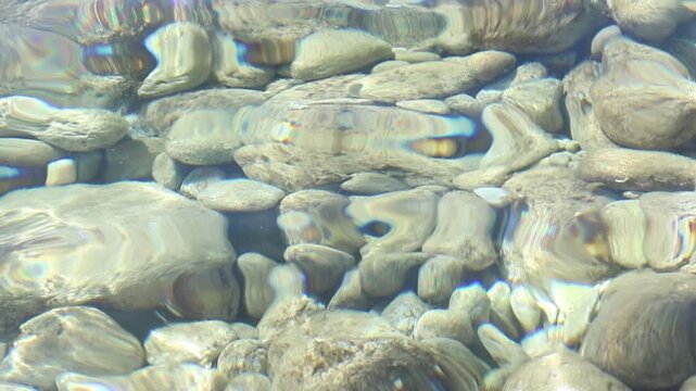 Crystal-clear coastal waters with smooth pebbles and stones beneath the surface. Tranquil summer seascape with gentle ripples captured as a serene underwater backdrop for travel and vacation themes