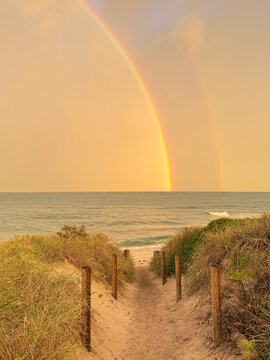 Rainbow sitting over ocean seen through fenced beach walkway