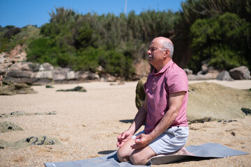Elderly man sitting on the beach meditating and doing yoga