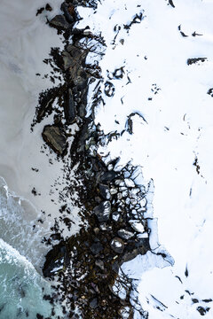 Aerial view of the rugged coastline with stark contrasts between the dark rocks and the bright snow-covered land, Leknes, Nordland, Norway.