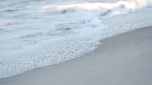 Gentle waves at the beach. Video shows calm ocean waves rolling onto sandy shore, with soft foam washing over the beach in a soothing rhythm.