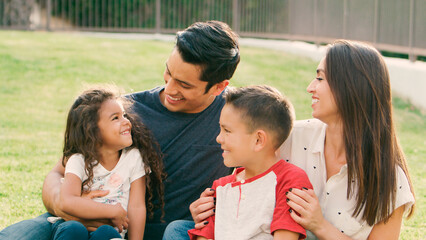 Smiling Family Sitting On Grass Outdoors In Park Together