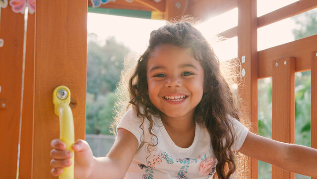 Portrait Of Smiling Young Girl Climbing On Equipment In Playground